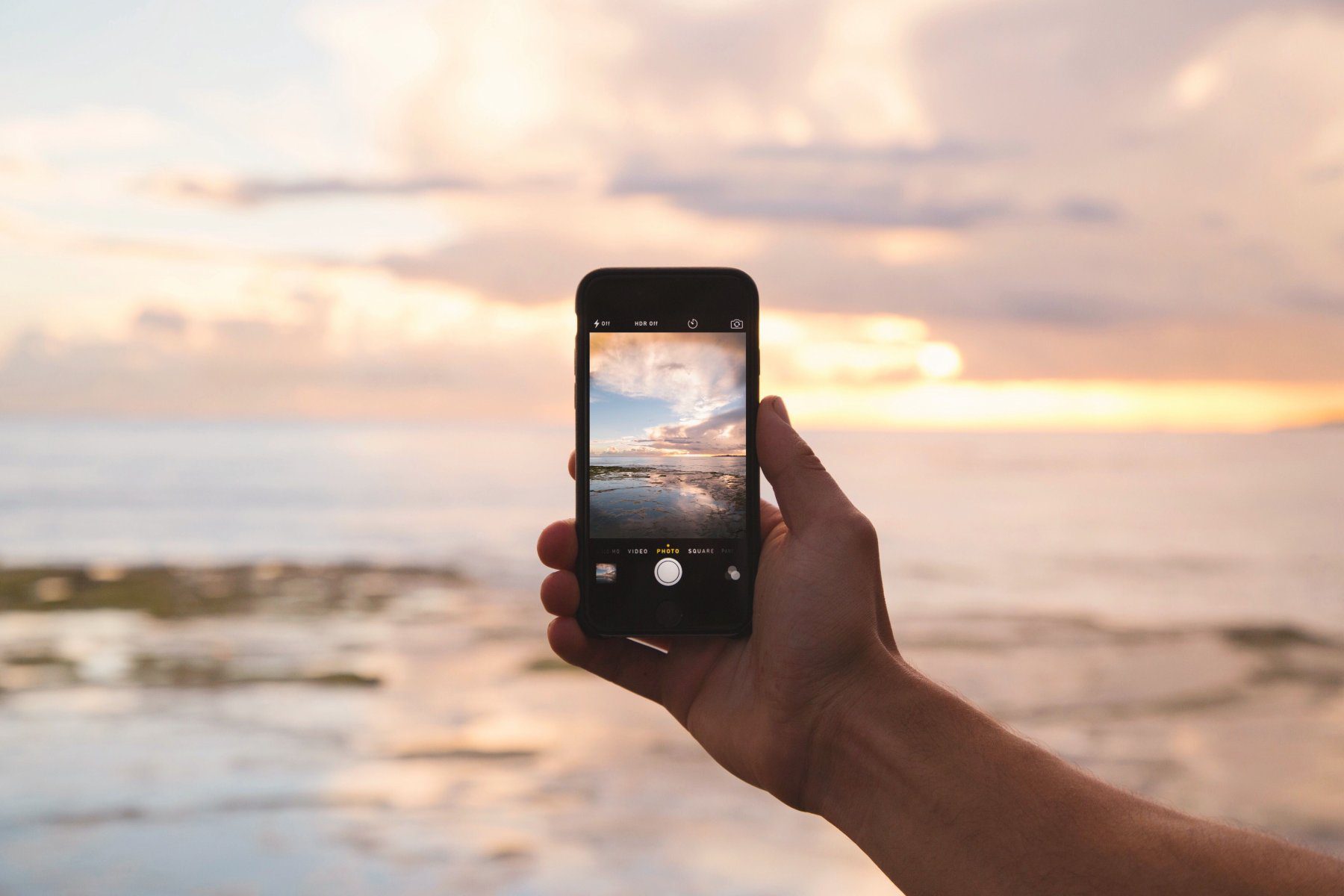 Mano sosteniendo un móvil fotografiando un atardecer en la playa